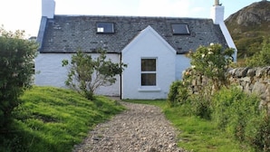A white house with a steeply pitched roof, a small front porch, and a gravel path leading to the entrance. - Harbour (Isle of Colonsay)