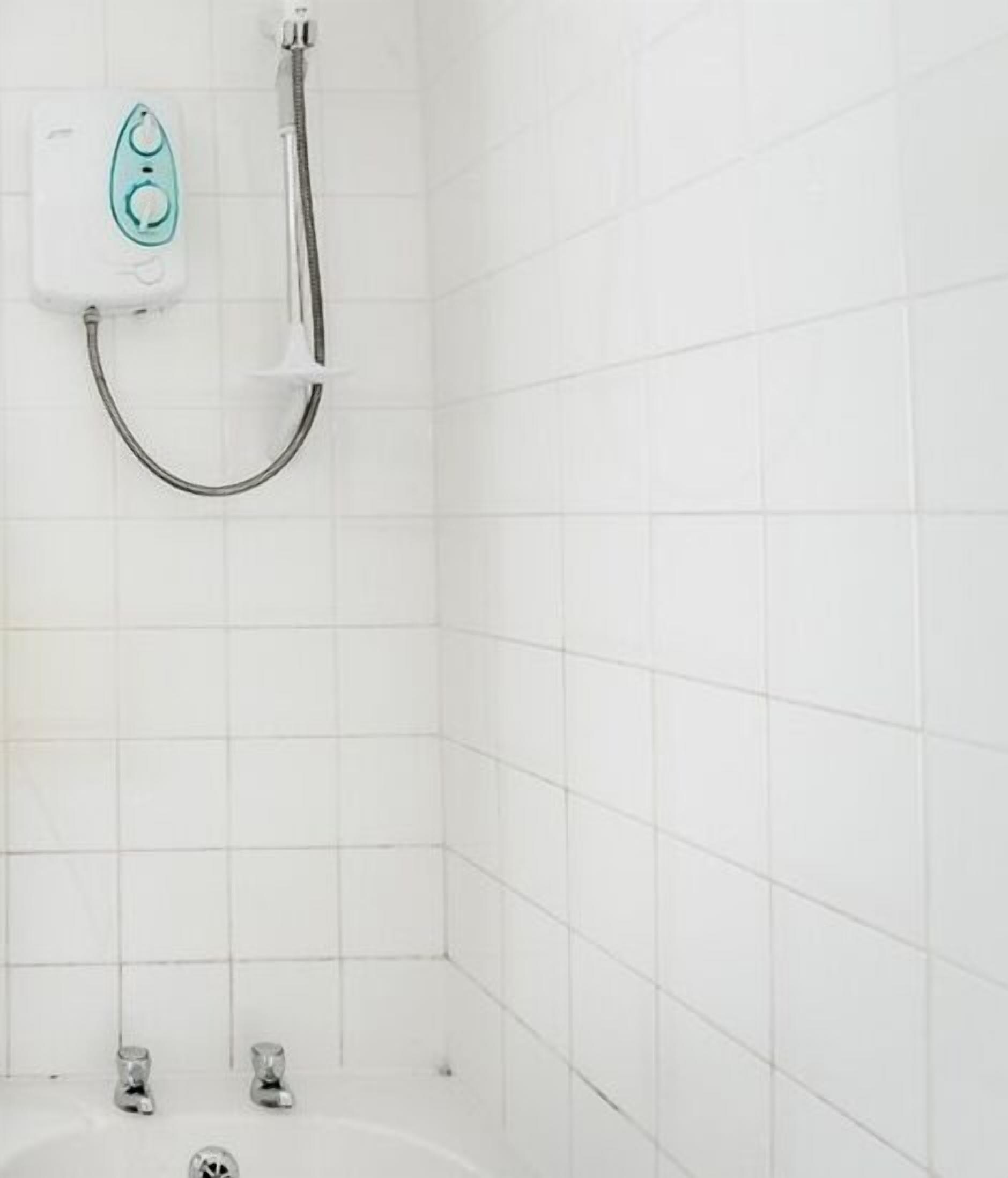 A bathroom with white tiled walls, a shower with a handheld showerhead, and a bathtub with two faucets.
