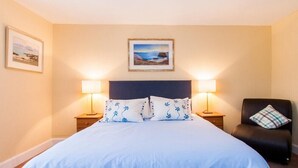 A hotel room with a large bed, two bedside lamps, a chair with a pillow, and two framed pictures on the wall. - Harbour (Isle of Colonsay)