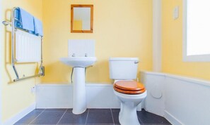 Un baño con un lavabo blanco, un inodoro con asiento de madera y un espejo en la pared.