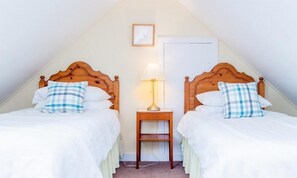 Una habitación con dos camas de madera, cada una con un cojín de cuadros, una mesita de noche con una lámpara y un cuadro enmarcado en la pared.