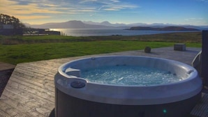 Ein Whirlpool auf einer Holzterrasse mit Blick auf einen See und Berge.
