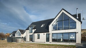 Ein modernes, zweistöckiges Haus mit großen Fenstern, einem geneigten Dach und einem sichtbaren Schornstein.