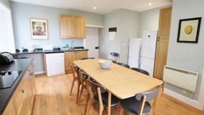A compact kitchen with wooden cabinets, a white refrigerator, and a dining table with chairs. - Tobaroran (Isle of Colonsay)