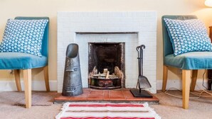 A cozy living room with a white brick fireplace, two blue upholstered chairs with matching pillows, a striped rug, and a metal fireplace poker. - Tobaroran (Isle of Colonsay)