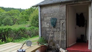 Un bâtiment en pierre avec une table en bois, une canne à pêche et une plante en pot.