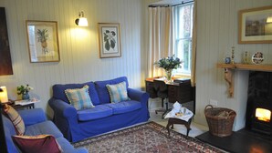 Un salon avec un canapé bleu, un tapis à motifs, une cheminée et des œuvres d’art encadrées accrochées au mur.