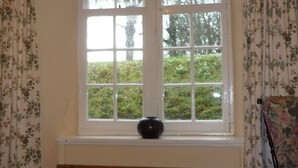 Una habitación con un ventanal grande, un banco de madera y una silla con estampado floral.