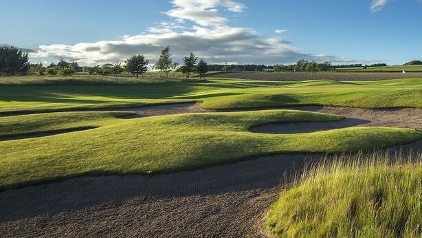 Ein Golfplatz mit gepflegtem Rasen, Sandbunkern und blauem Himmel.
