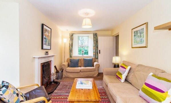 A cozy living room with a fireplace, a sofa, a coffee table, and a window with curtains.