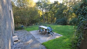 A stone pathway leading to a table and chairs set outdoors, surrounded by greenery and trees.