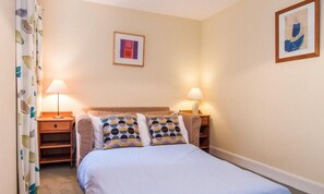 A bedroom with a bed, two bedside tables, a nightstand, a wall-mounted picture, and a curtain with a leaf pattern.
