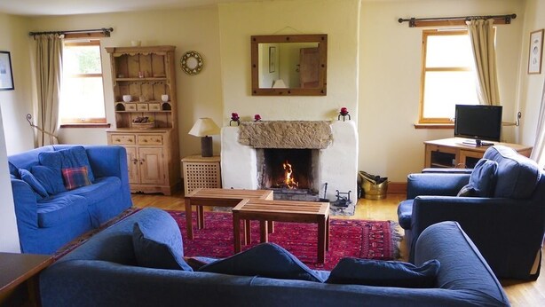 A cozy living room with a fireplace, blue sofas, a wooden cabinet, and a television. - Bail nan Cnoc (Newtonmore)