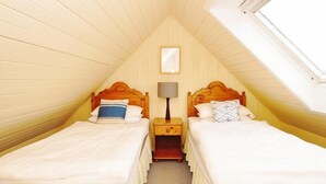 A small, cozy attic bedroom with two wooden beds, a nightstand with a lamp, and a window.