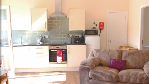 A compact kitchen with a microwave, oven, and a red oven mitt hanging on the oven handle.