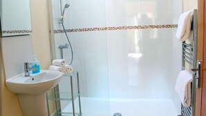 A modern bathroom with a glass shower enclosure, a sink with a soap dispenser, and a towel rack.
