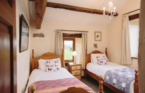 A cozy bedroom with two wooden beds, a nightstand, a window with curtains, and a chandelier. - Garth Cottage (Hot Tub) (Brampton)