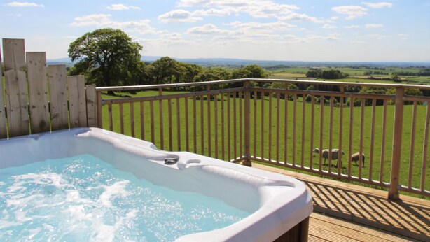 A hot tub on a wooden deck with a view of a green field and sheep. - Garth Cottage (Hot Tub) (Brampton)