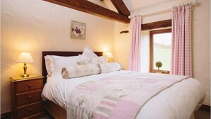 A bedroom with a wooden headboard, two bedside lamps, a quilt, and a window with pink curtains. - Garth Cottage (Hot Tub) (Brampton)