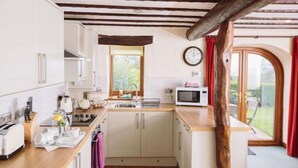 A kitchen with white cabinets, a wooden ceiling, a microwave, and a window with curtains. - Garth Cottage (Hot Tub) (Brampton)
