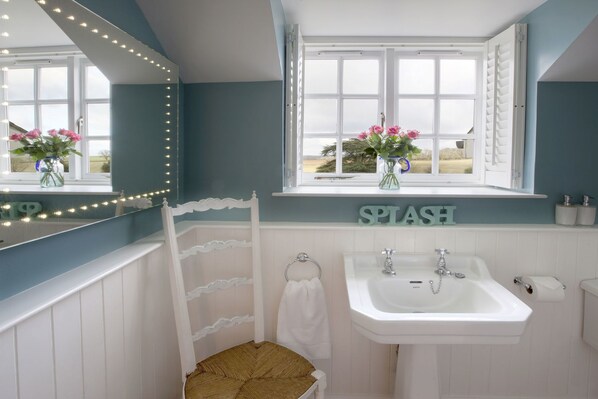 A bathroom with a white sink, a mirror with lights, a window with flowers, and a sign that says "SPITASH".