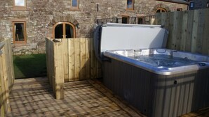 A hot tub in a wooden deck area with stone walls and arched windows. - Gelt Cottage (Hot Tub) (Brampton)