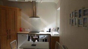 A compact kitchen with wooden cabinets, a white countertop, and a built-in dishwasher. - Little Dunbar (Dumfries)