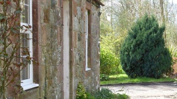 A stone building with a window and a well-maintained garden with a large bush. - Little Dunbar (Dumfries)