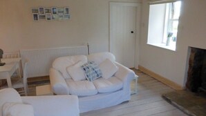 A living room with a white sofa, a small table, and a fireplace. - Little Dunbar (Dumfries)