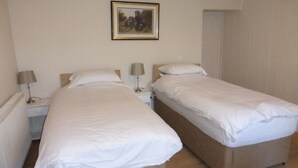 A hotel room with two single beds, a bedside table with a lamp, and a framed picture on the wall. - Little Dunbar (Dumfries)