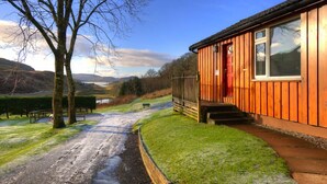A wooden cabin with a red door, a small porch, and a view of a valley. - Ash lodge (Oban)