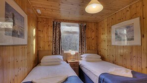 A wooden cabin room with two beds, a window with curtains, and framed pictures on the walls. - Ash lodge (Oban)