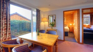 A room with a wooden dining table, chairs, a bed, and a window with curtains. - Ash lodge (Oban)