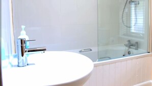 A bathroom with a white sink, chrome faucet, and a glass shower enclosure. - Ivy Garden Cottage (Alexandria)