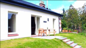 A white building with a black roof, a sign reading "Ivy Cottage," and a patio with wooden furniture. - Ivy Garden Cottage (Alexandria)