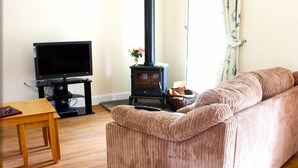 A living room with a sofa, a television, a wooden table, and a wood-burning stove. - Ivy Garden Cottage (Alexandria)