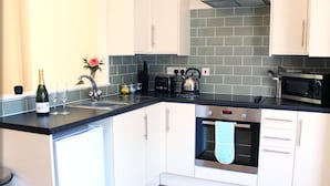 A modern kitchen with white cabinets, a stainless steel oven, a microwave, and a black countertop. - Ivy Garden Cottage (Alexandria)