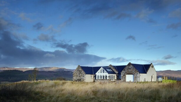 A stone house with a white facade and a blue roof, set against a mountainous backdrop. - Mountain View Lodge 375948 (Kingussie)