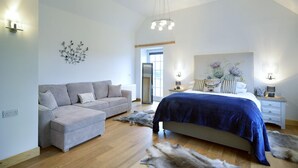A bedroom with a bed, a sofa, a nightstand, and a wall-mounted light fixture. - Mountain View Lodge 375948 (Kingussie)