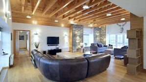 A spacious living room with a curved leather sofa, a stone accent wall, and a wooden ceiling. - Mountain View Lodge 375948 (Kingussie)
