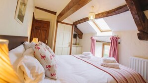 A bedroom with a wooden ceiling, a bed with white bedding, a chandelier, and a window with curtains. - Low Barn (Brampton)
