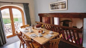 A dining area with a wooden table set for four, a bench, and a view of the outdoors through a glass door. - Low Barn (Brampton)