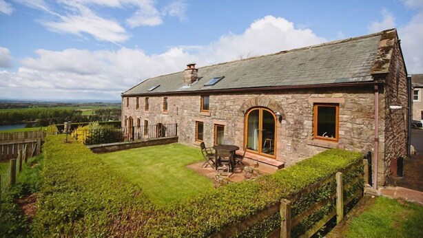 A stone house with a well-maintained lawn, a patio with outdoor furniture, and a scenic view of the countryside. - Low Barn (Brampton)