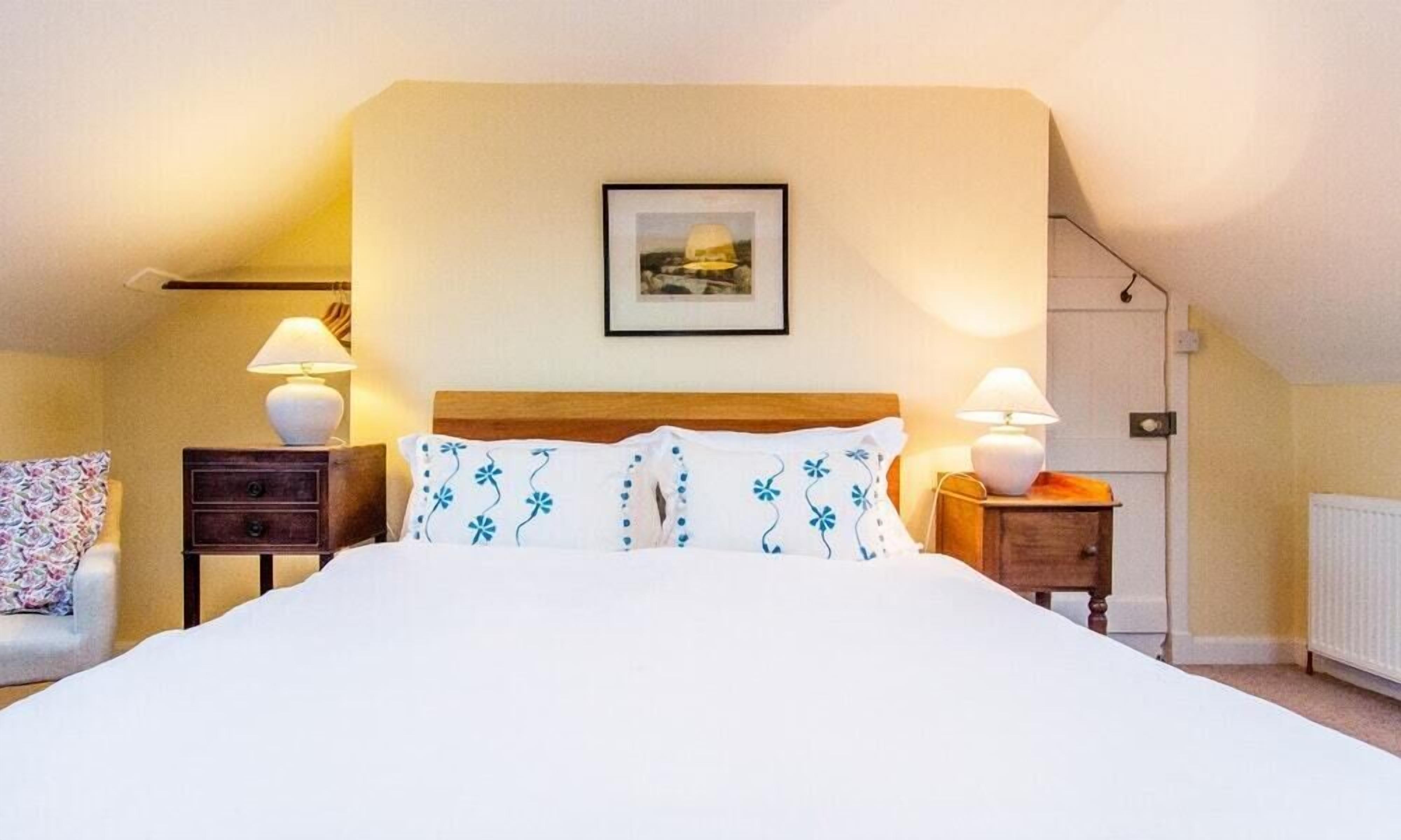 A bedroom with a large bed, two bedside tables with lamps, a chair, and a framed picture on the wall.
