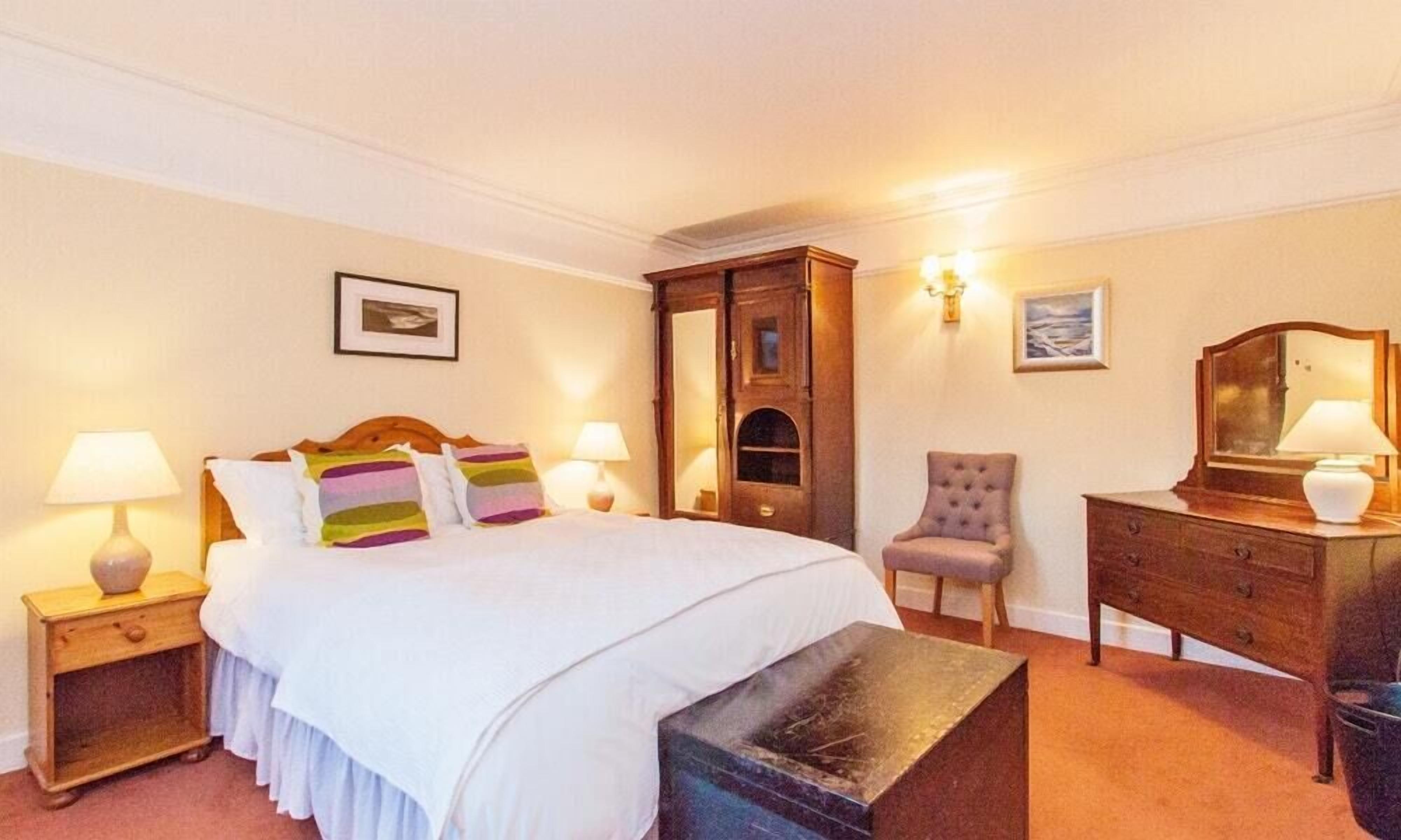 Un dormitorio ordenado con cama, mesitas de noche, cómoda y una silla.