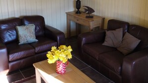 A living room with two brown leather sofas, a wooden coffee table with a red polka-dotted vase of yellow flowers, a wooden side table with a lamp, and framed pictures on the wall. - Allt Bronach (Newtonmore)
