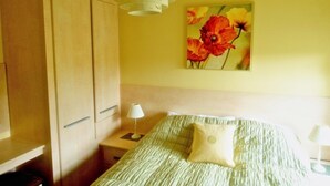 A bedroom with a bed, a nightstand, a lamp, a wardrobe, and a painting of flowers on the wall. - Allt Bronach (Newtonmore)