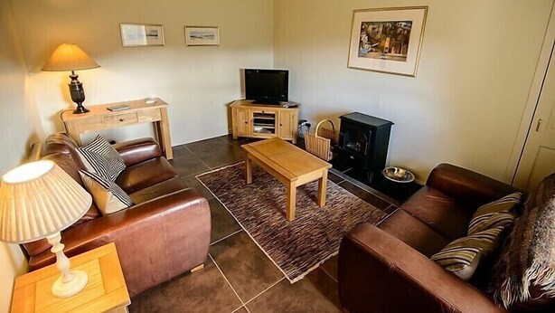 A living room with a sofa, a coffee table, a TV, a fireplace, and a lamp. - Allt Bronach (Newtonmore)