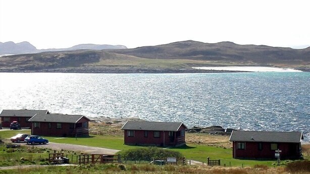 A coastal area with several small cabins, a clear view of the sea, and distant hills. - Spruce (Ullapool)