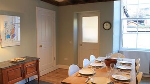A dining room with a wooden table set for four, chairs, a wooden sideboard, a clock on the wall, and a window with blinds. - 10 Murray Park  375840 (St. Andrews)